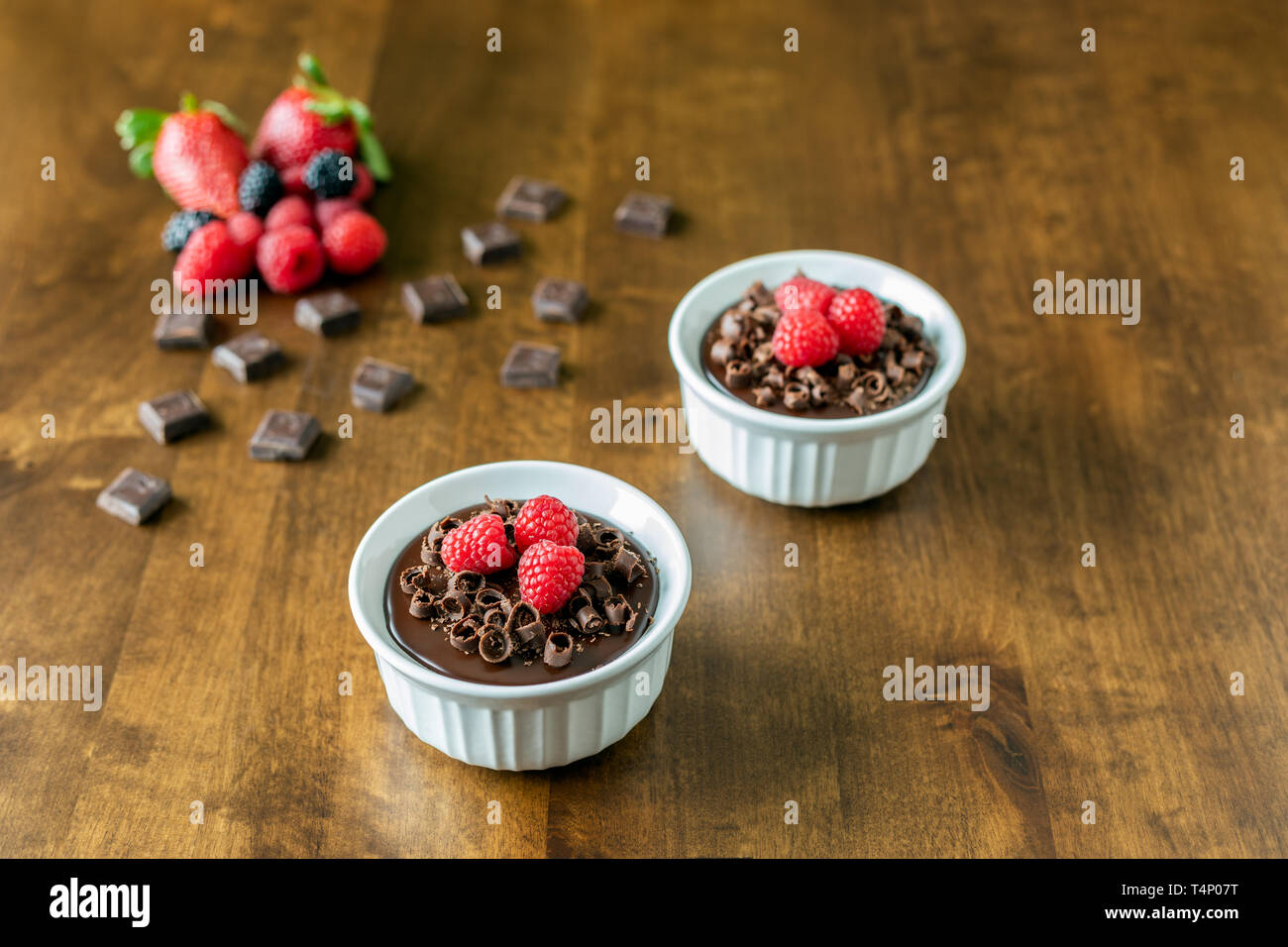 A decadent Chocolate Mousse Cake with chocolate ganache and topped with Raspberries, Blackberries and chocolate curls on a wood table in a ramekin dis Stock Photo