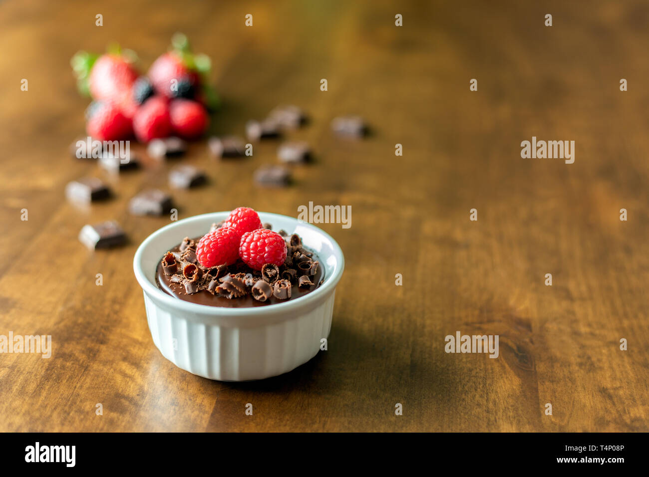 A decadent Chocolate Mousse Cake with chocolate ganache and topped with Raspberries, Blackberries and chocolate curls on a wood table in a ramekin dis Stock Photo