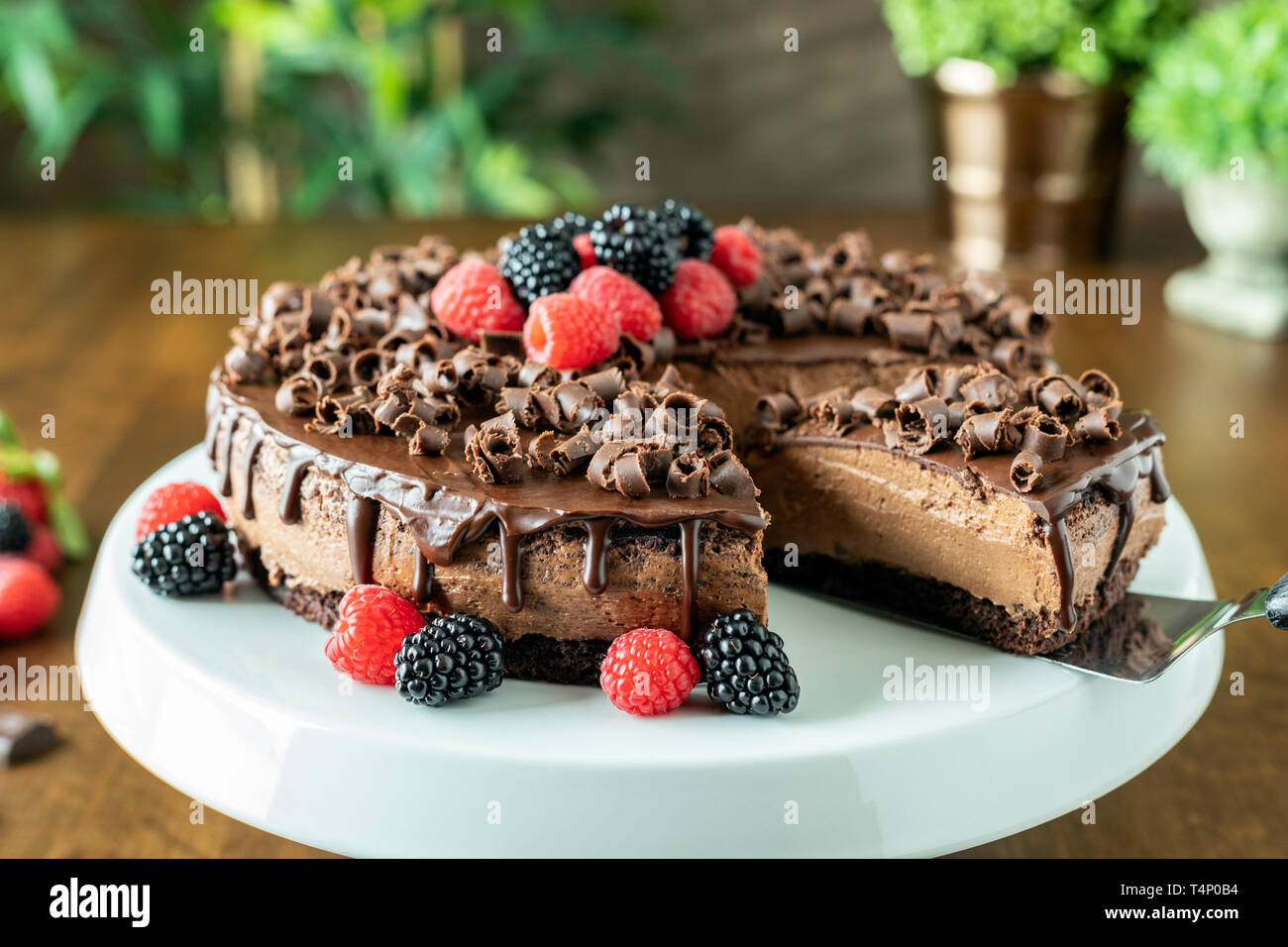 A decadent Chocolate Mousse Cake with chocolate ganache and topped with Raspberries, Blackberries and chocolate curls on a wood table Stock Photo