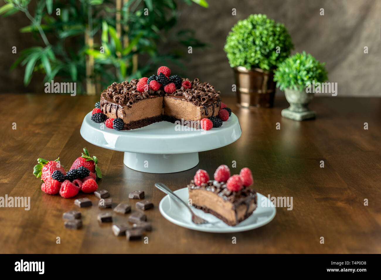 A decadent Chocolate Mousse Cake with chocolate ganache and topped with Raspberries, Blackberries and chocolate curls on a wood table Stock Photo
