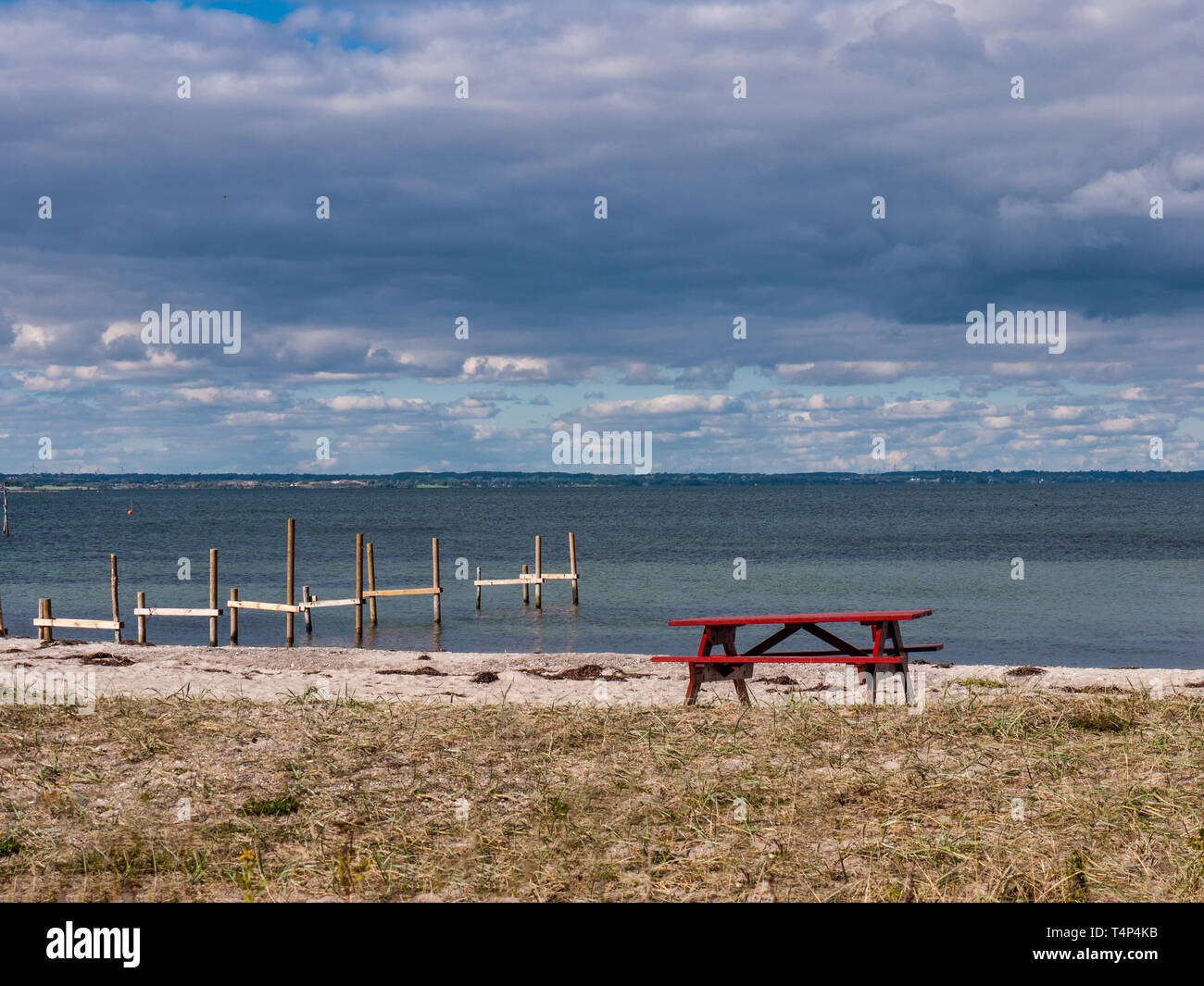 Red picnic table on a sandy beach with the Baltic Sea in the background on the island Langeland, Denmark Stock Photo