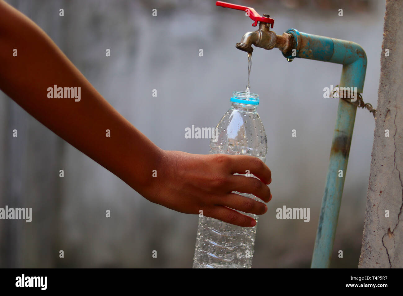 Young hand collecting water with a plastic bottle from an old slow