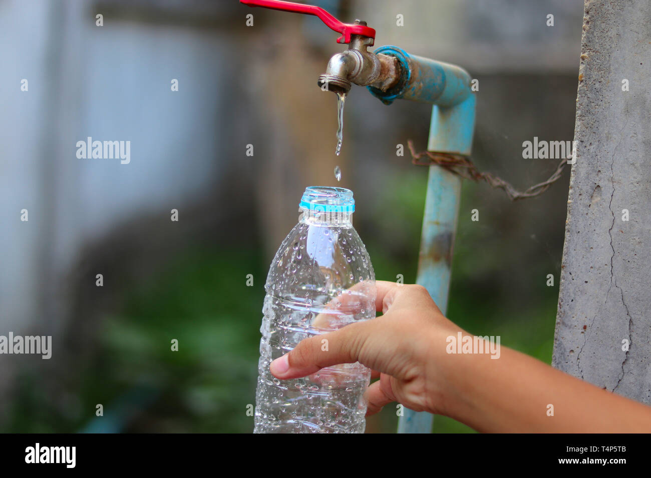 Young hand is collecting water with a plastic bottle from an old slow flowing water tap with great patience - water shortage - save water concept. Stock Photo