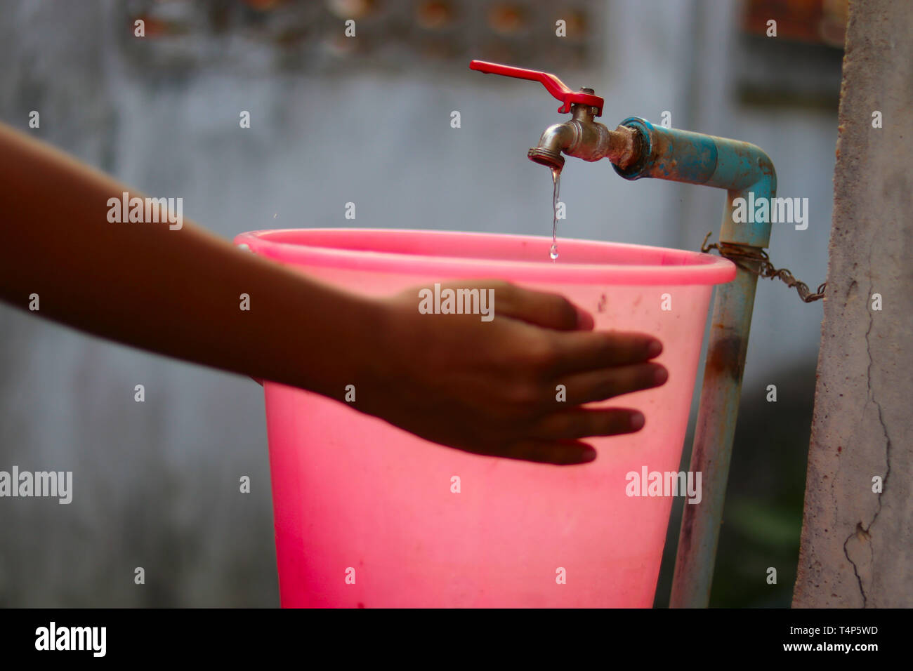 Young hands collecting water with a plastic bucket from an old slow