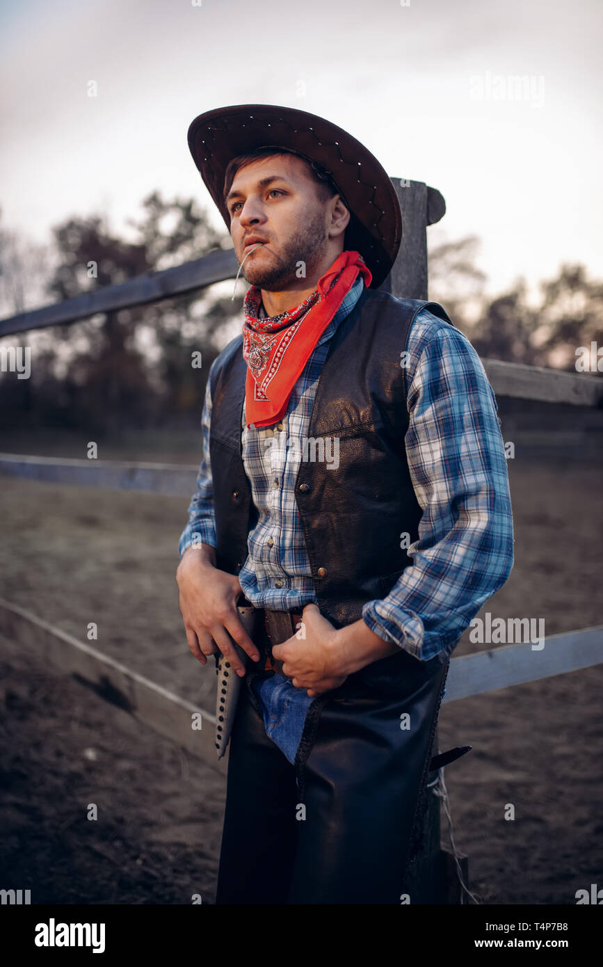 Young cowboy in leather jacket and hat poses against horse corral
