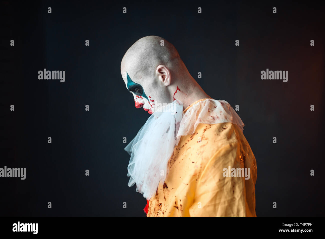 Sad bloody clown with makeup in carnival costume, side view. Crazy maniac, scary monster Stock Photo