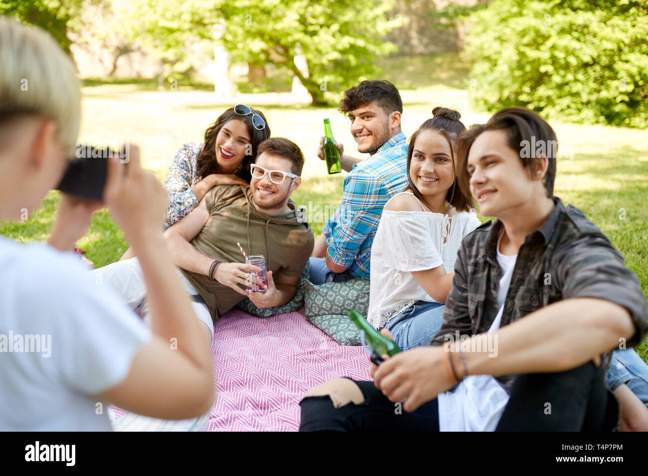 friendship, leisure and technology concept - woman with camera photographing his friends drinking non alcoholic drinks at picnic in summer park Stock Photo