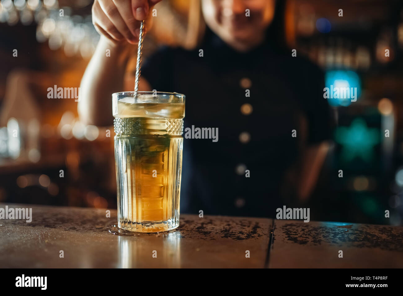 Female barman stir the drink in a glass. Woman bartender mixing at the bar counter in pub. Barkeeper occupation Stock Photo