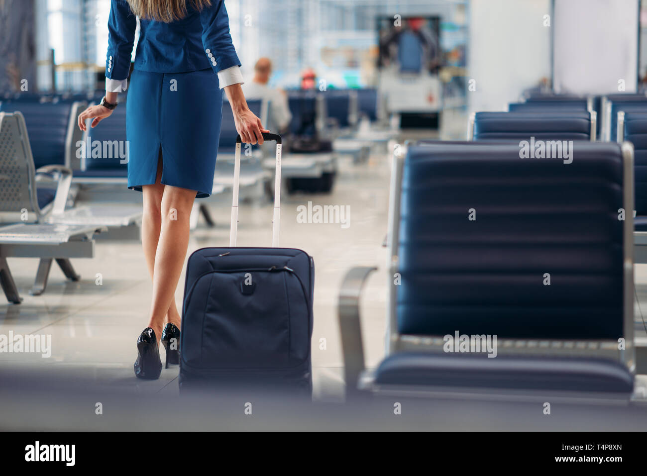 Air hostess with suitcase going between seat rows in airport