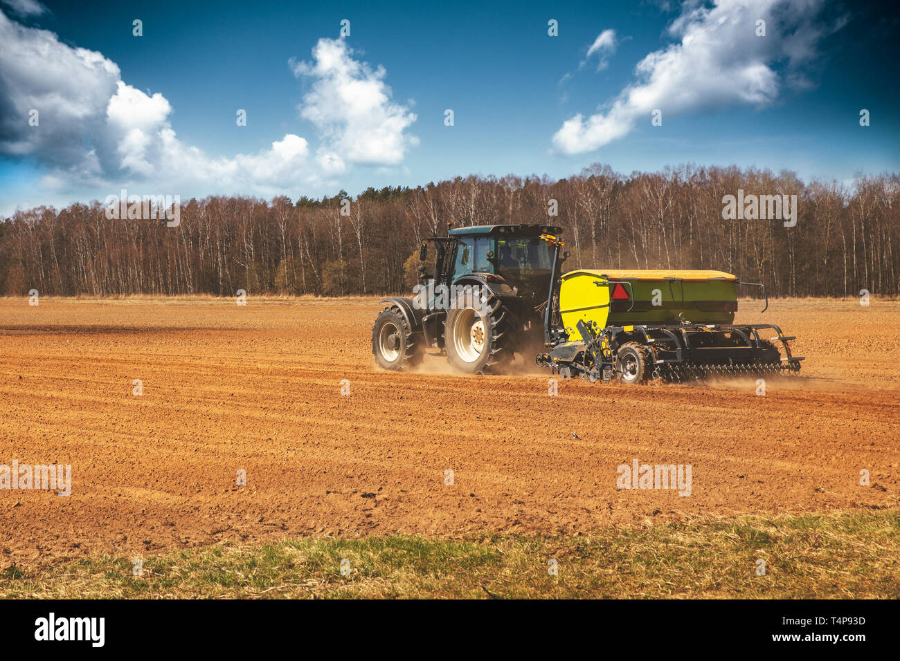 farming - farmer with tractor on the field seeding sowing crops in spring Stock Photo