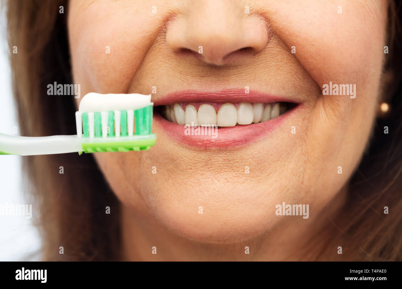 dental care and hygiene people concept - close up of smiling senior woman with toothbrush brushing her teeth over white background Stock Photo