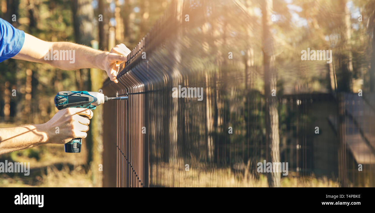 fencing - worker installing metal wire mesh fence panel Stock Photo