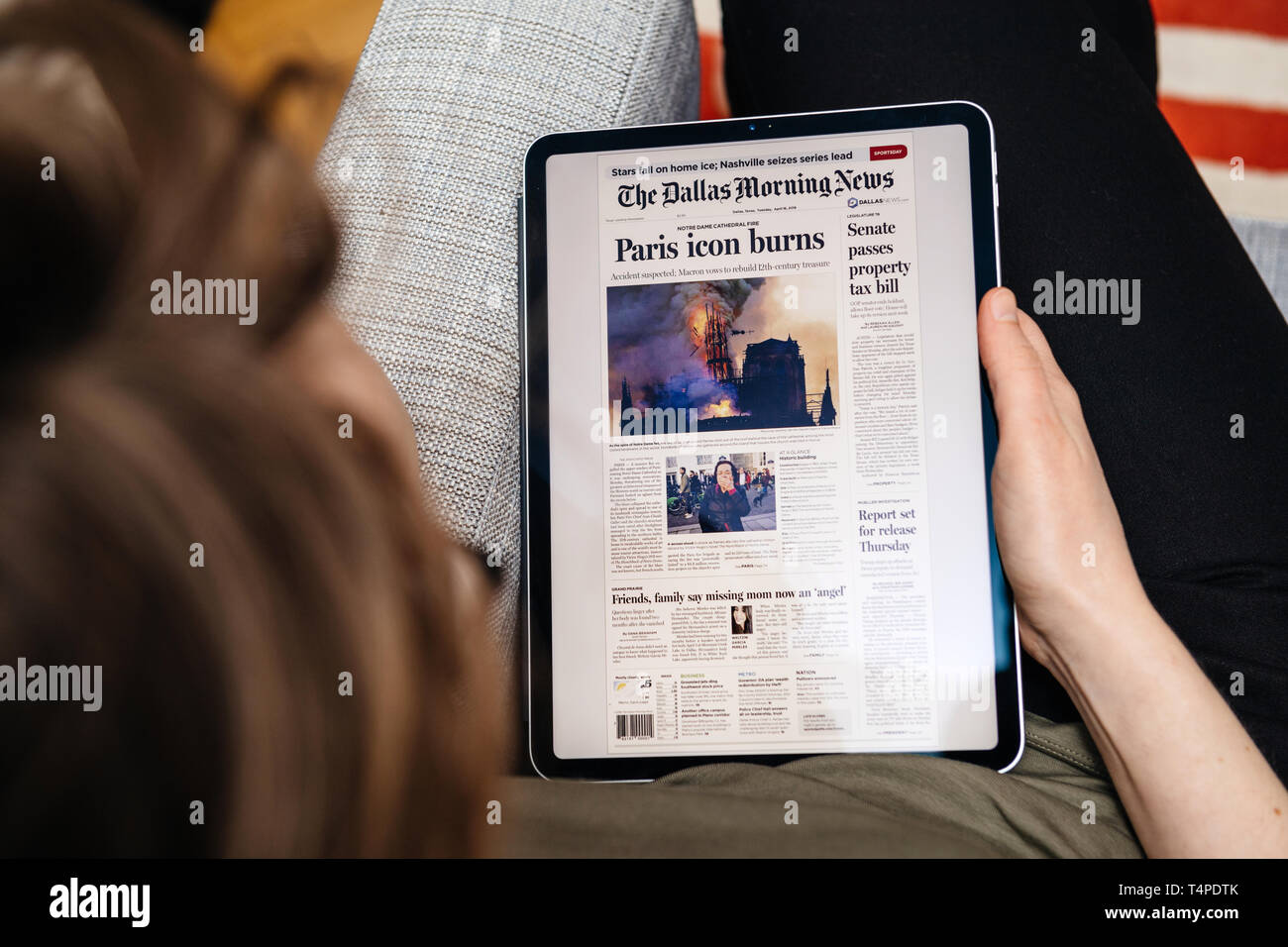 Paris, France - Apr 15, 2019: Woman reading The Dallas Morning News on iPad Pro Apple News Plus digital newspaper featuring breaking news on cover French Notre-Dame Cathedral on fire causing damages  Stock Photo