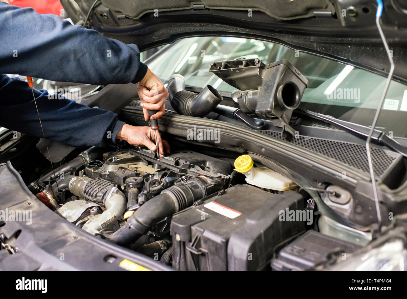 Mechanic working on a car engine doing repairs or servicing maintenance in a closeup view of his hands using a screwdriver Stock Photo