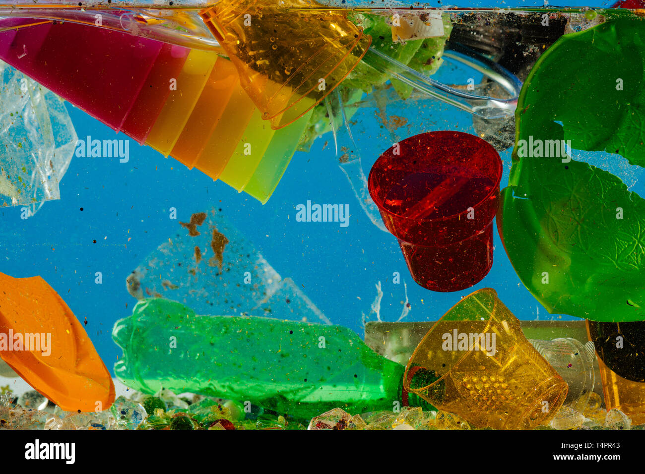 Immersing crumpled bottle. Disposal colorful plastic cups floating