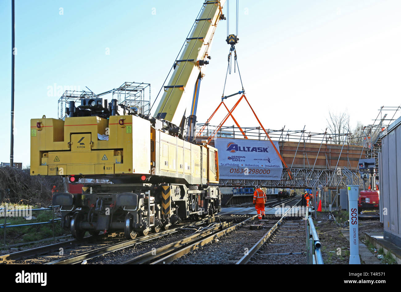 A railway-mounted Kirow crane lifts a temporary scaffolding footbridge into place at Feltham Station, Middlesex during a weekend railway closure. Stock Photo