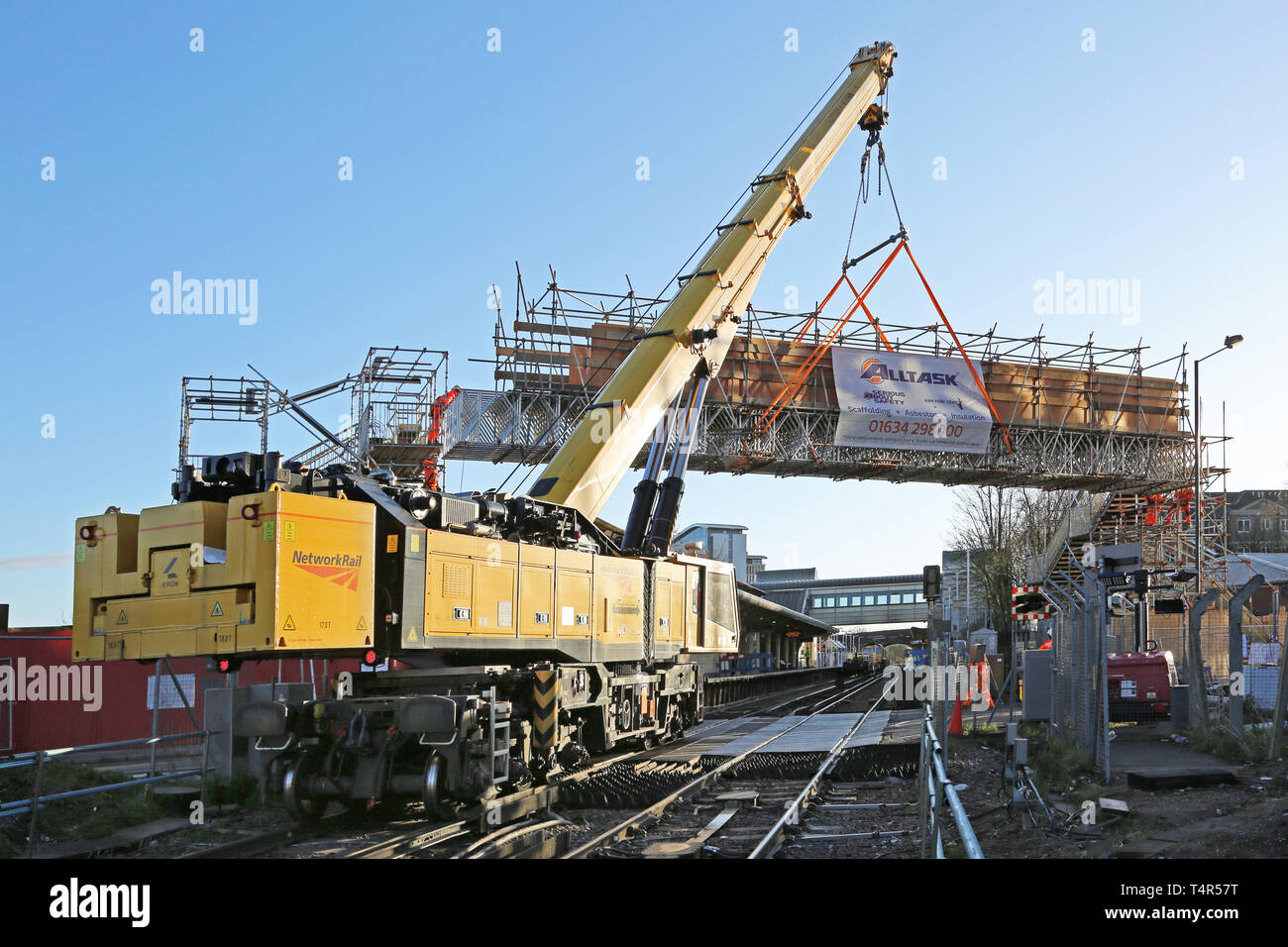 A railway-mounted Kirow crane lifts a temporary scaffolding footbridge into place at Feltham Station, Middlesex during a weekend railway closure. Stock Photo