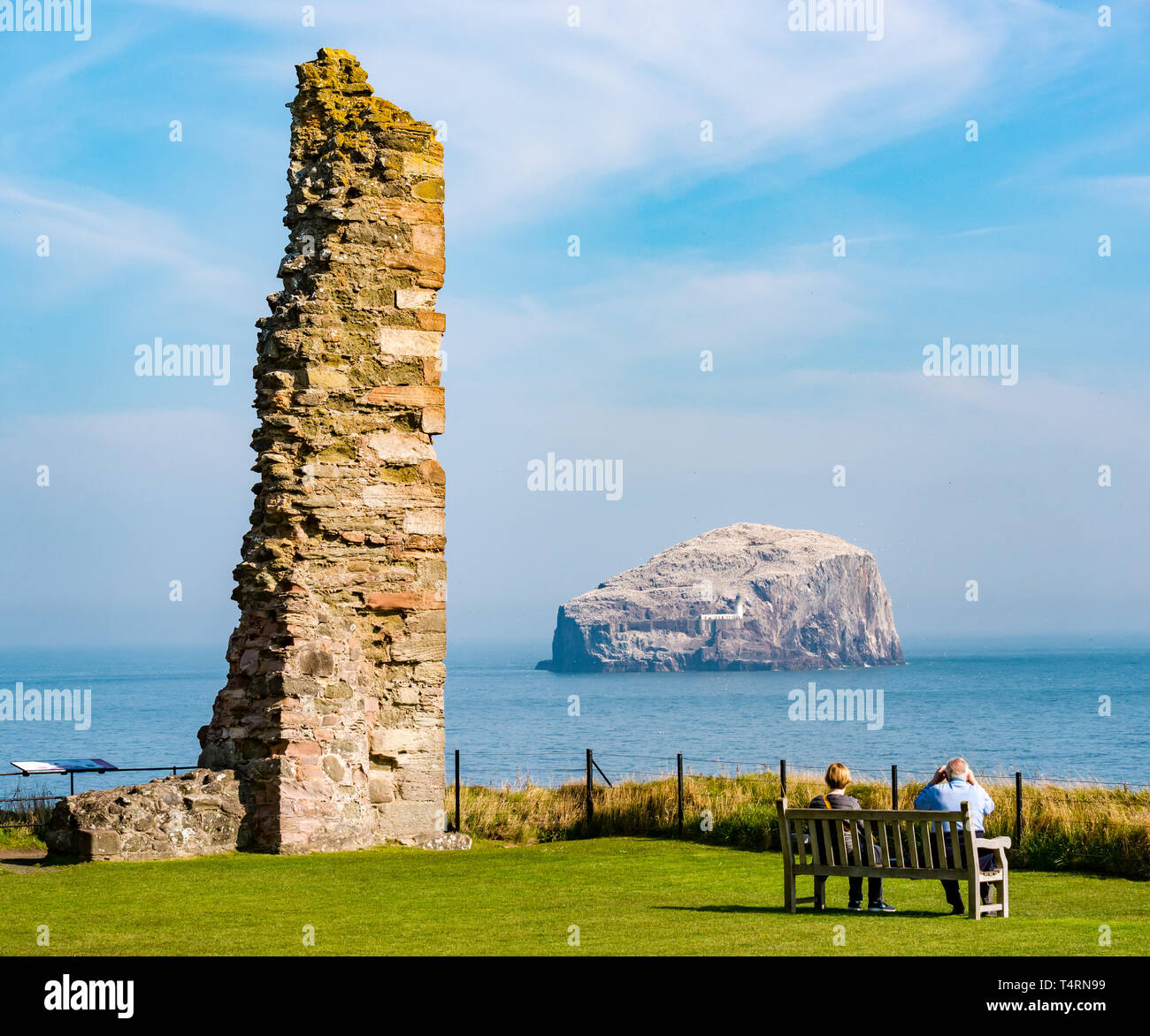 Tantallon Castle, North Berwick, East Lothian, Scotland, United Kingdom, 19th April 2019. UK Weather: Historic Environment Scotland's ruined 14th century castle. The ruined castle with a view of the largest Northern gannet colony on the Bass Rock in the Firth of Forth. The gannets are reuniting and building nests. A couple with binoculars sit on a bench to watch the seabirds Stock Photo