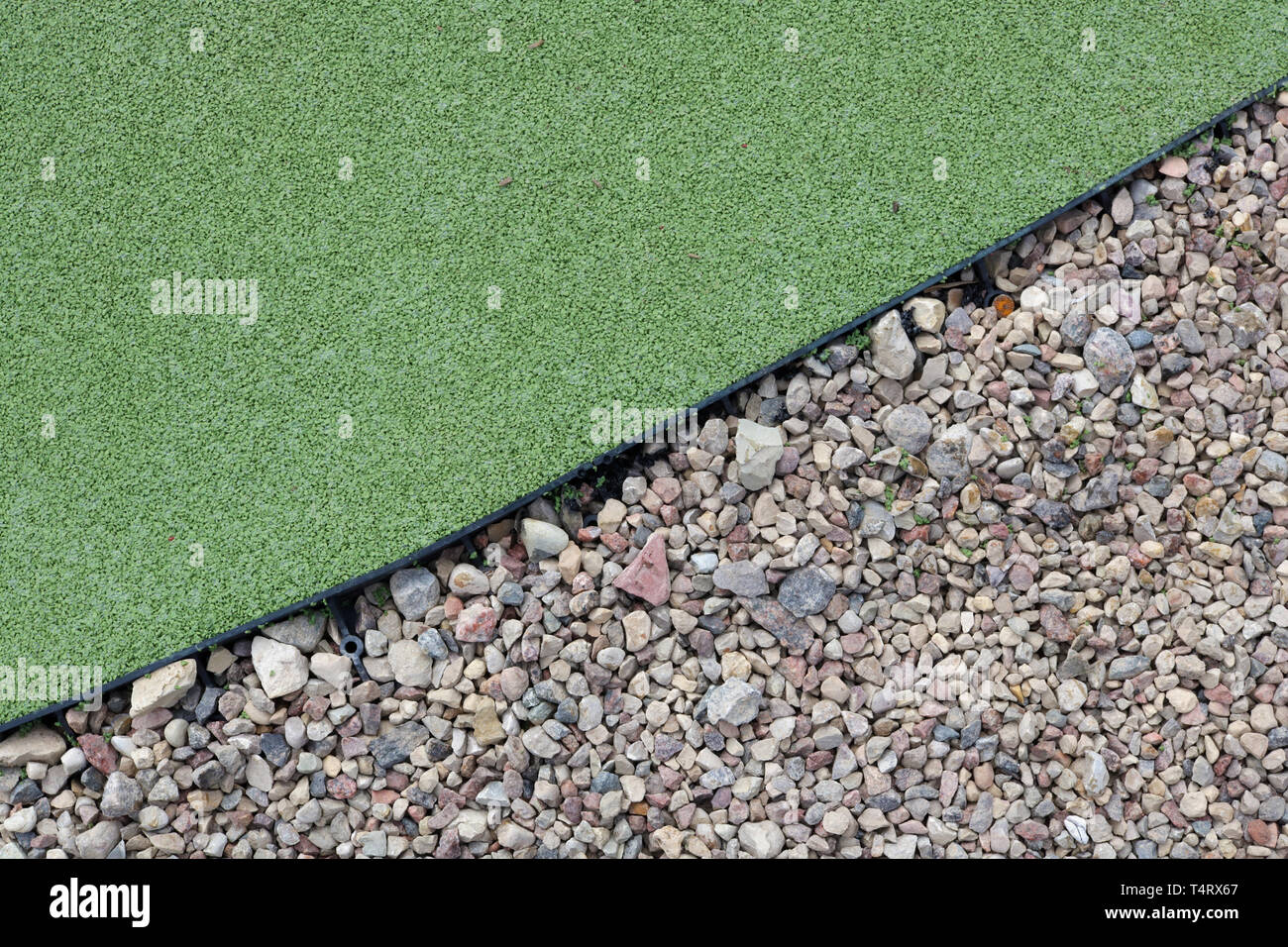 Plastic tape separates green soft rubber and small pebbles in a children's playground. Outdoor