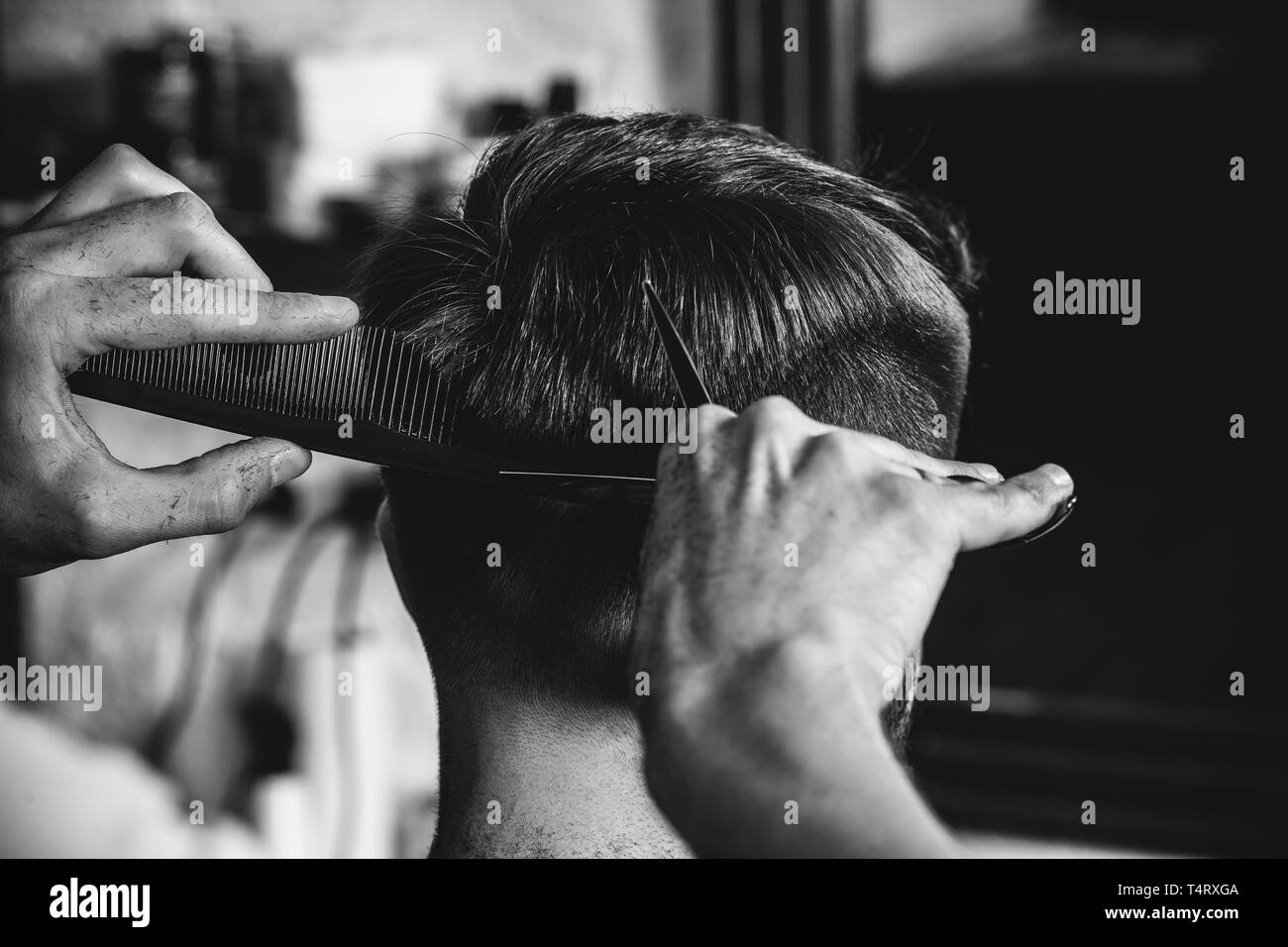 Young handsome barber making haircut for attractive bearded man at barbershop. Black and white or colorless photo. Hairstyle, salon, hairdresser, barber shop, lifestyle concept. Caucasian male models. Stock Photo