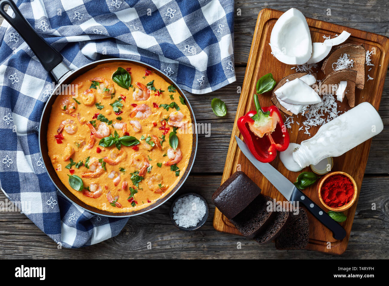 Shrimps in Coconut Sauce with blended vegetables in a skillet on a rustic wooden table with ingredients, camarao no leite de coco, brazilian recipe, v Stock Photo