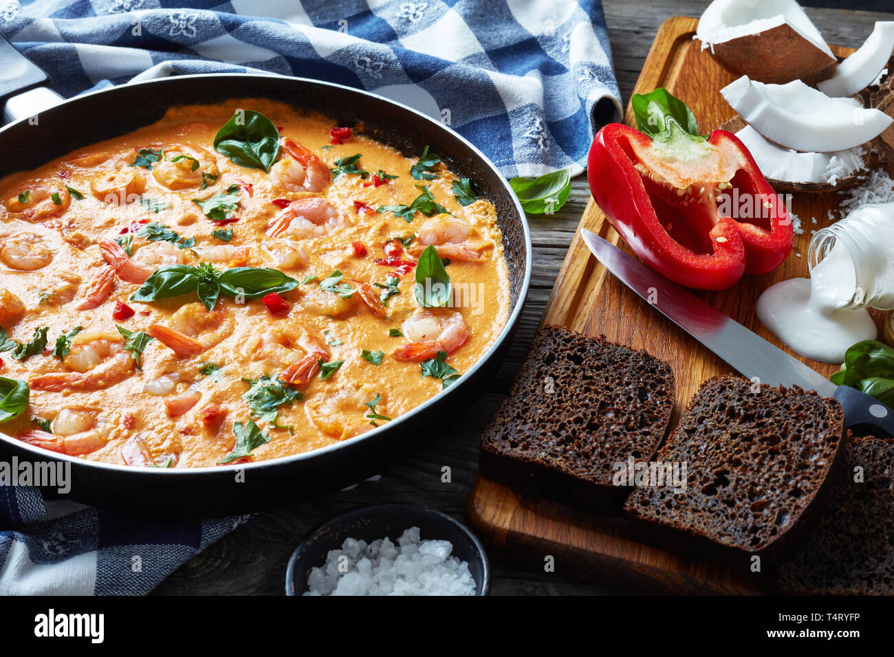 Shrimps in Coconut Sauce with blended vegetables in a skillet on a rustic wooden table with kitchen towel and ingredients, camarao no leite de coco, b Stock Photo
