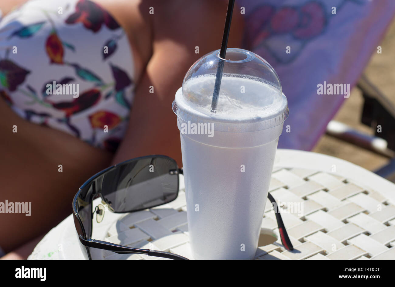 Greek coffee frappe in cup with foam near sunglasses on blurred background body part of woman with bra Stock Photo