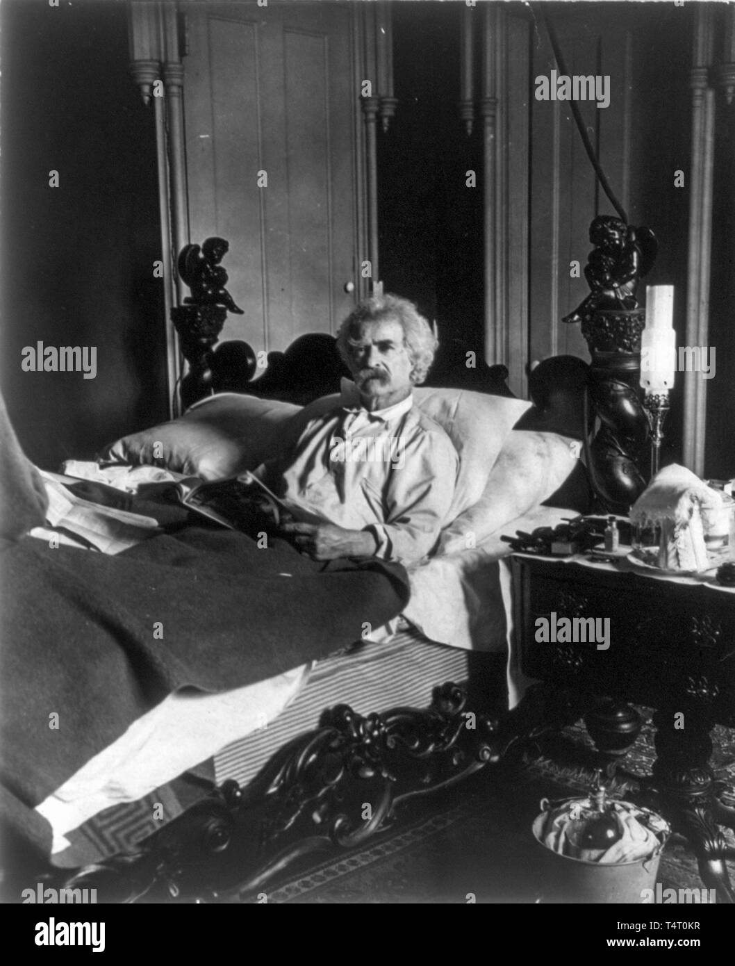 Mark Twain (1835-1910), lying in bed, holding magazine, 1906 Stock Photo