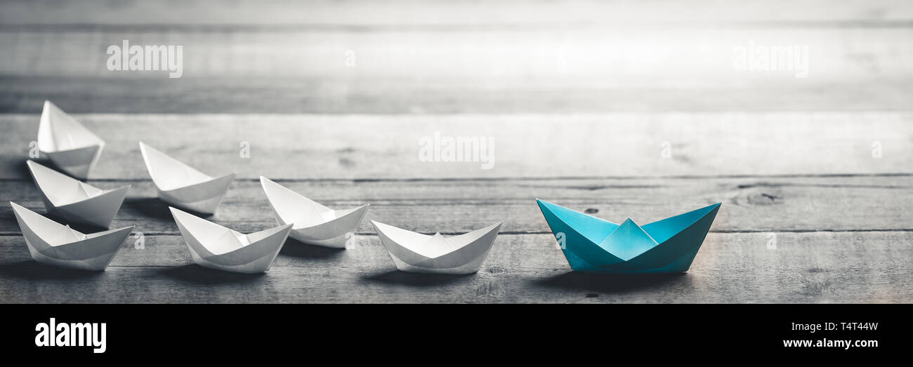 Blue Paper Boat Leading A Fleet Of Small White Boats On Wooden Table With Vintage Effect - Leadership Concept Stock Photo