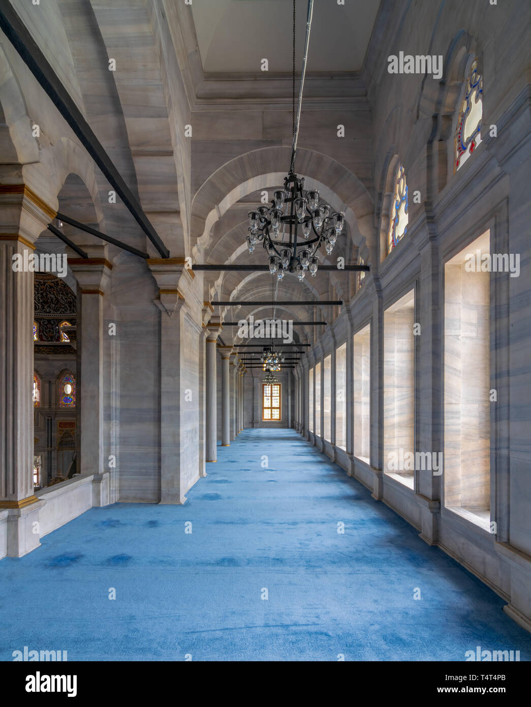 Passage in Nuruosmaniye Mosque, a public Ottoman Baroque style mosque, with columns, arches and floor covered with blue carpet lighted by side windows Stock Photo