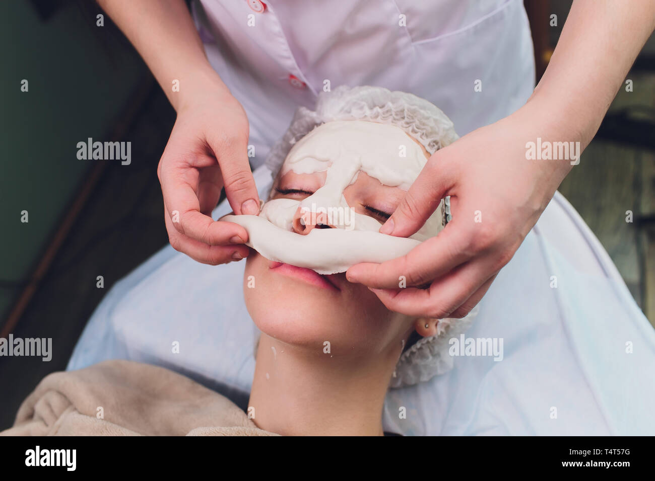 Facial procedures. Nice skilled cosmetician taking off a mask while doing a beauty procedure Stock Photo