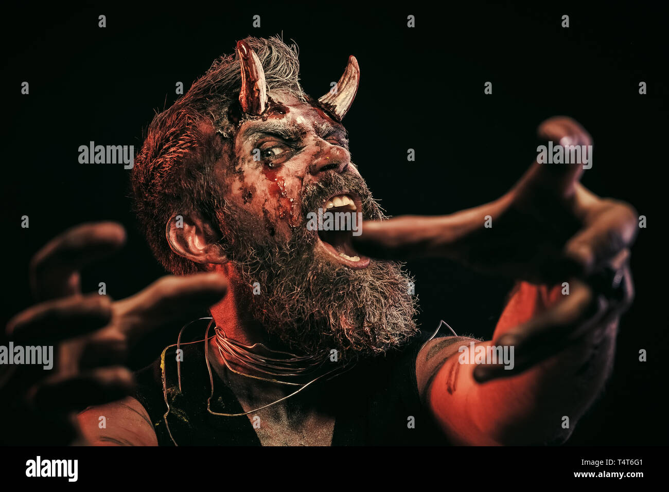 Halloween man devil satan with horns stretch zombie hands on black background. Chase, catching concept. Stock Photo