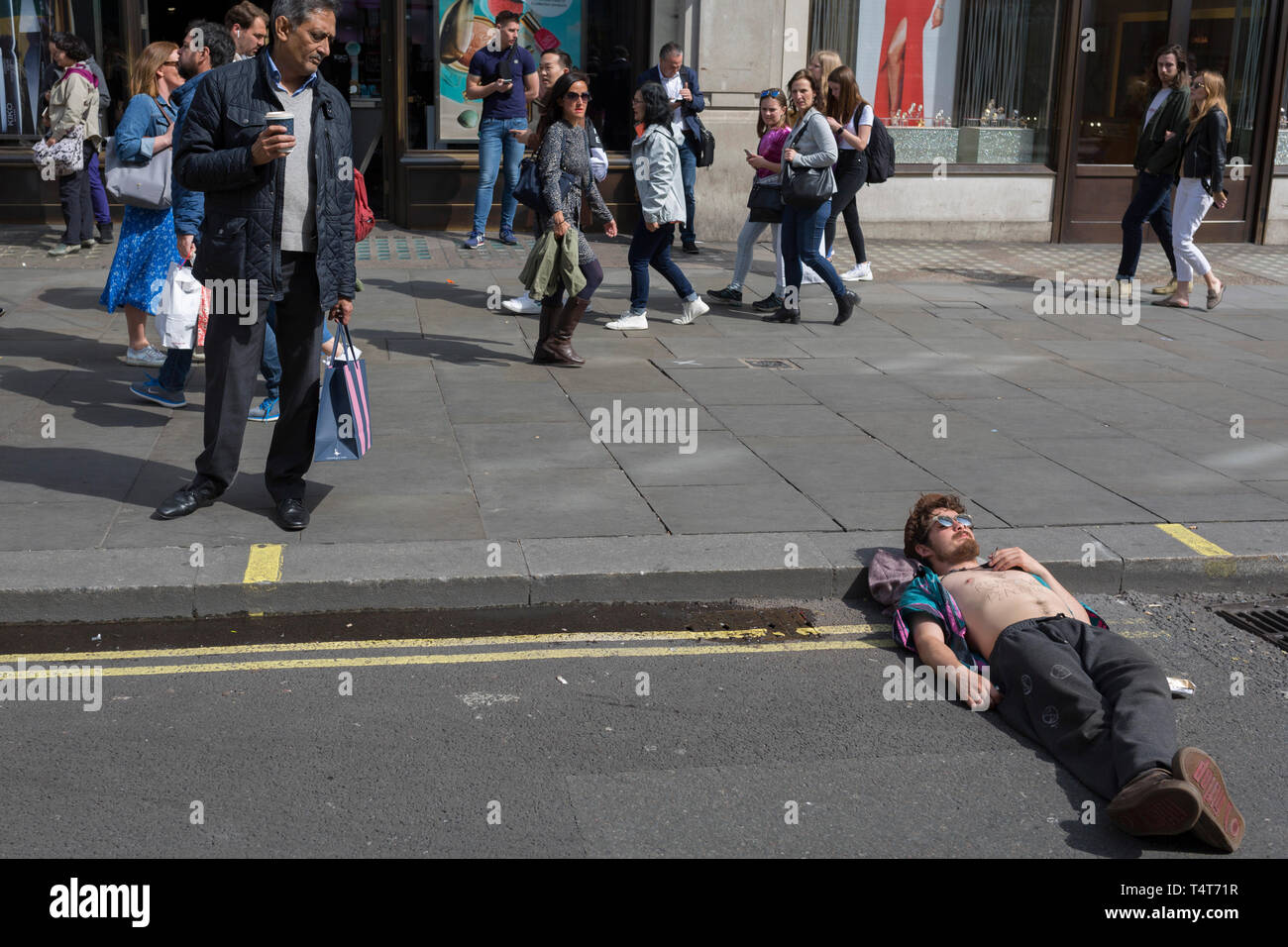 Passers-by look down on a young campaigner resting with his head on an ...