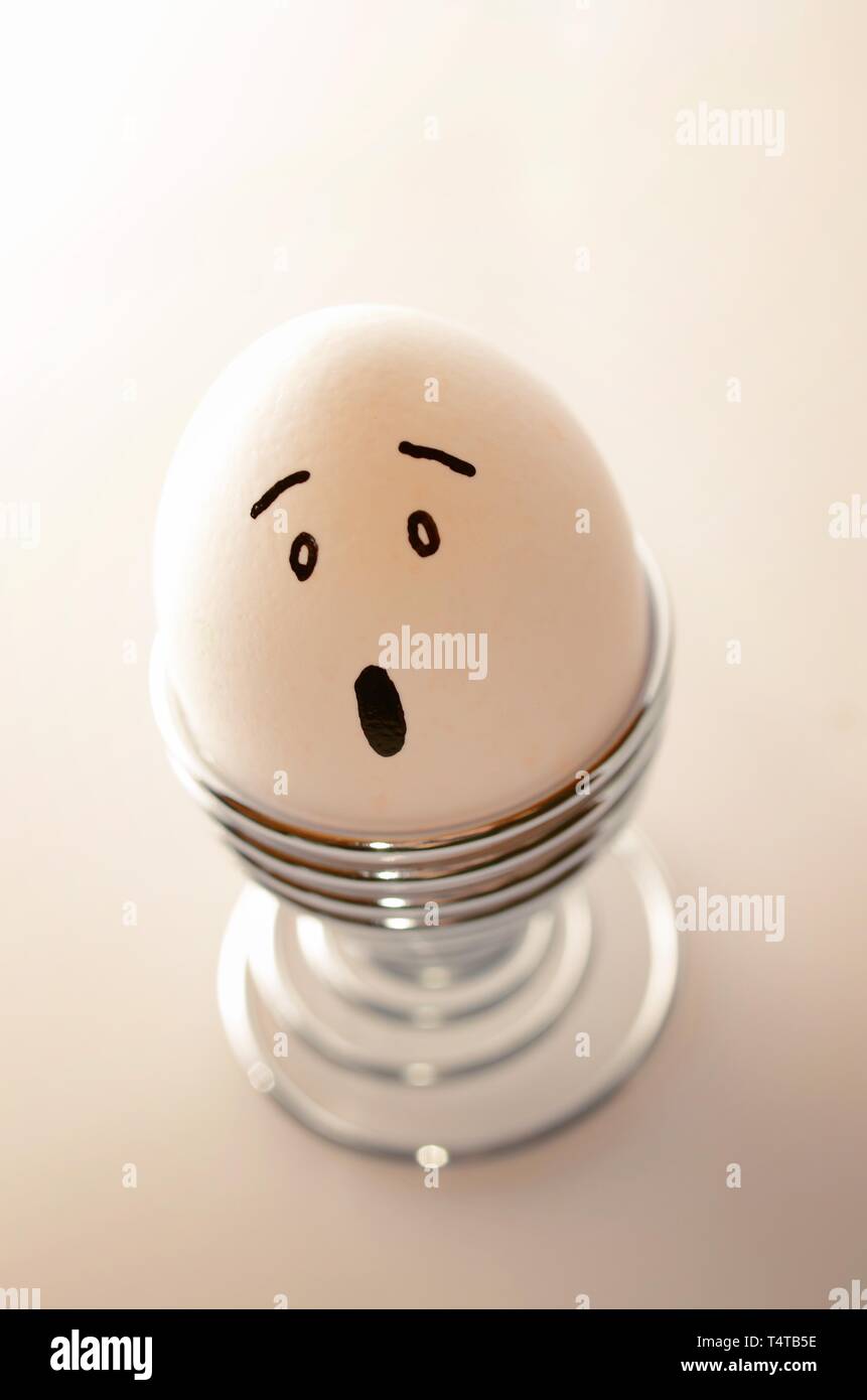 Single white, anthropomorph chicken egg in silver egg cup with surprised facial expression. Stock Photo