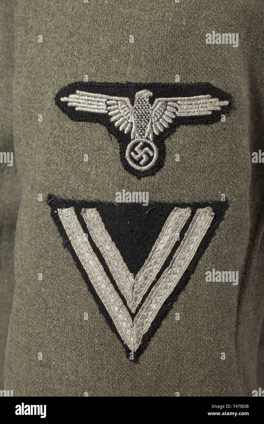 A field tunic M 43 for a Rottenführer of a signal unit of the SS Death's Head Regiment 3 'Theodor Eicke' depot piece SS cut with five button holes and two belt holes, made of field-grey woollen cloth with metal buttons, late production series with thin grey and green lining, the loops for the belt hooks made of the same material, faded stamps. The upper collar partly loosened near the collar hook. Black collar patches with horizontally embroidered death's head and silver rank braiding, respectively, black slip-on shoulder boards with lemon-yellow piping, sleeve chevron with, Editorial-Use-Only Stock Photo