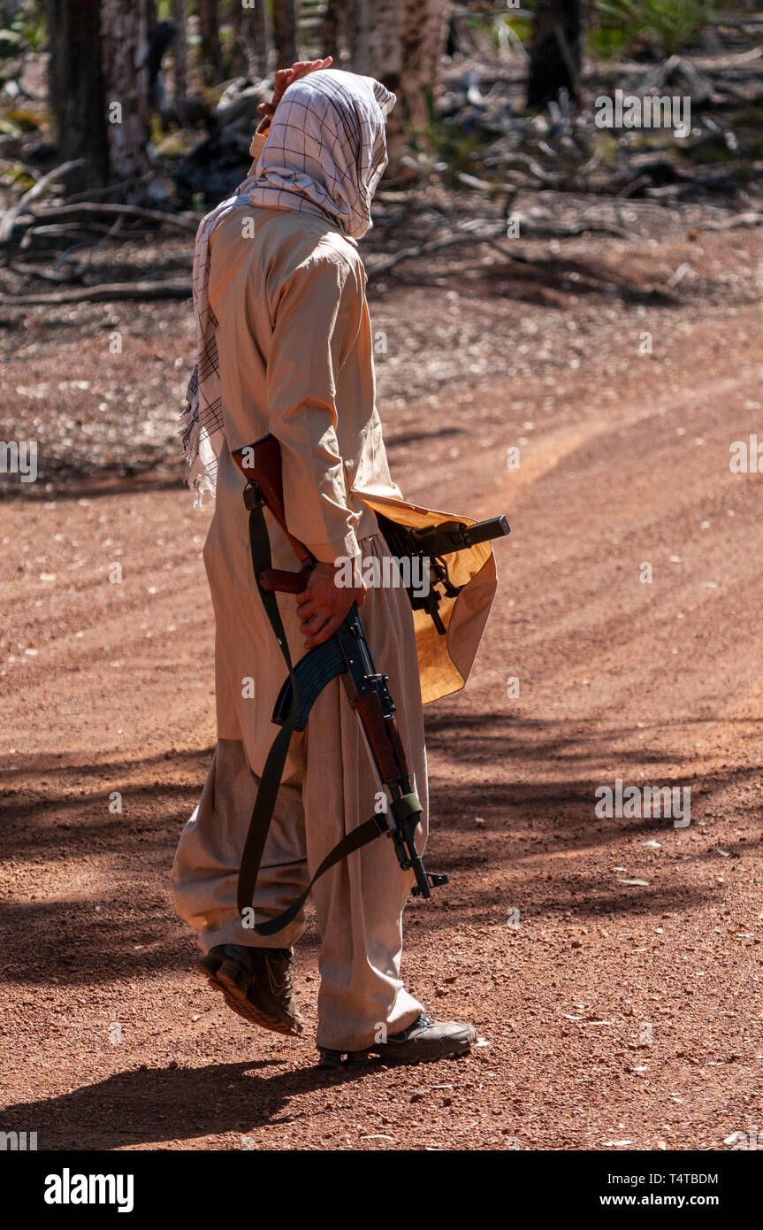 Rear view portrait view, of an ISIS soldier with a Kalashnikov AK47 assault rifle and sub machine gun. Stock Photo