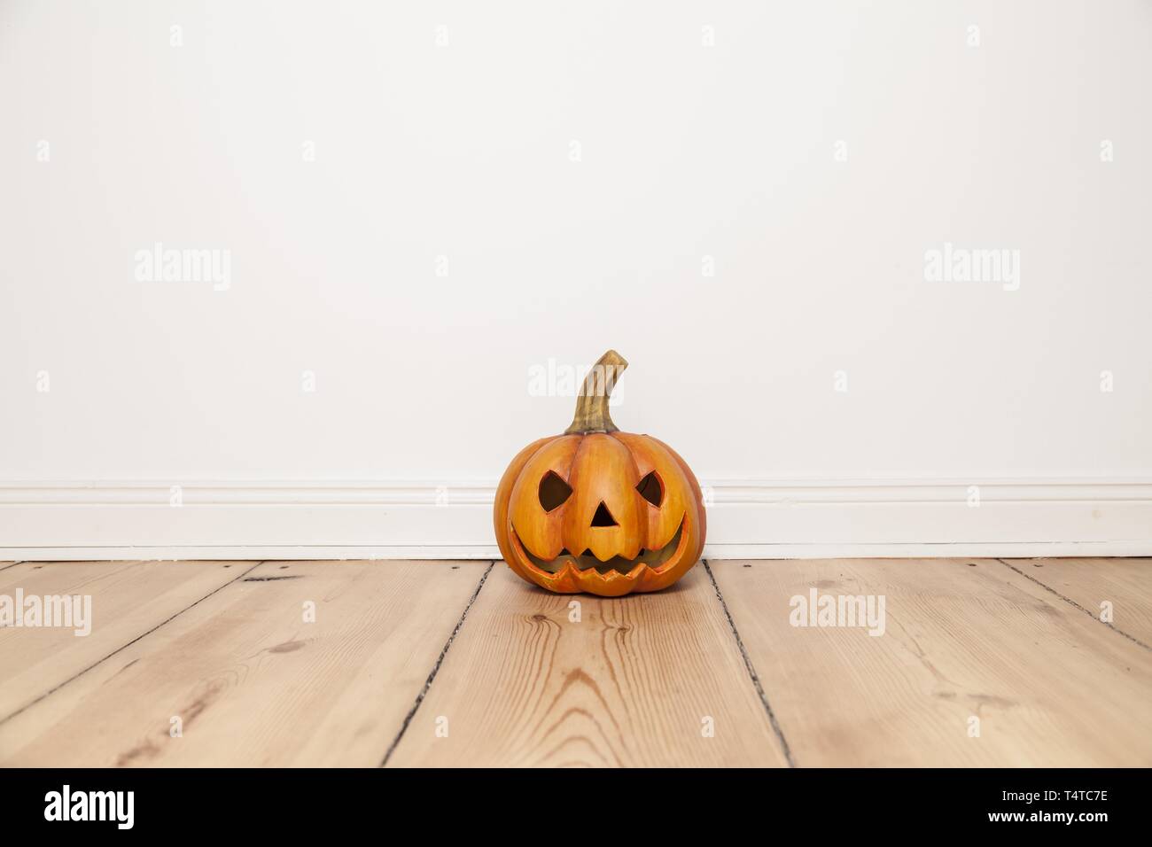 Grinning clay pumpkin on wooden floor, Halloween Stock Photo