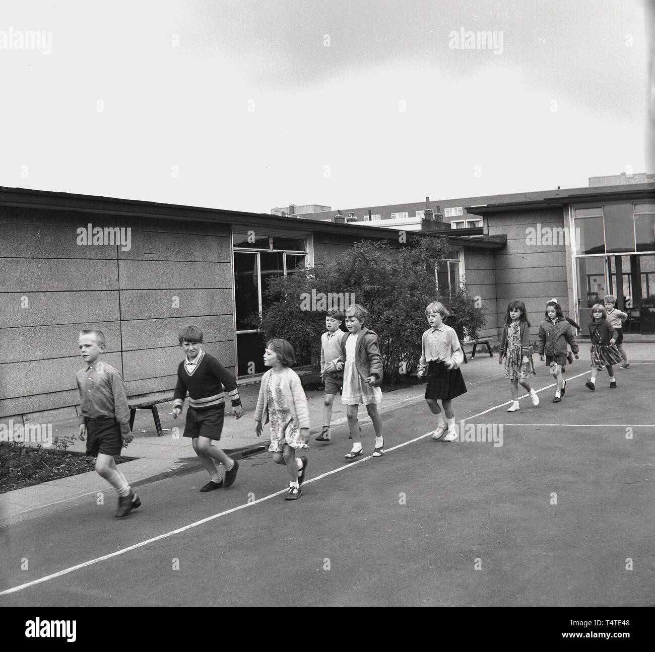 1960s, historical, primary school children walking around the perimeter of the school playground