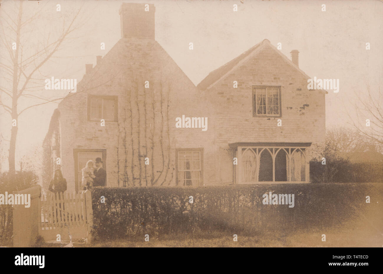 Vintage Photographic Postcard Showing an Historic British Detached House With a Father and His Two Children in The Front Garden. Stock Photo