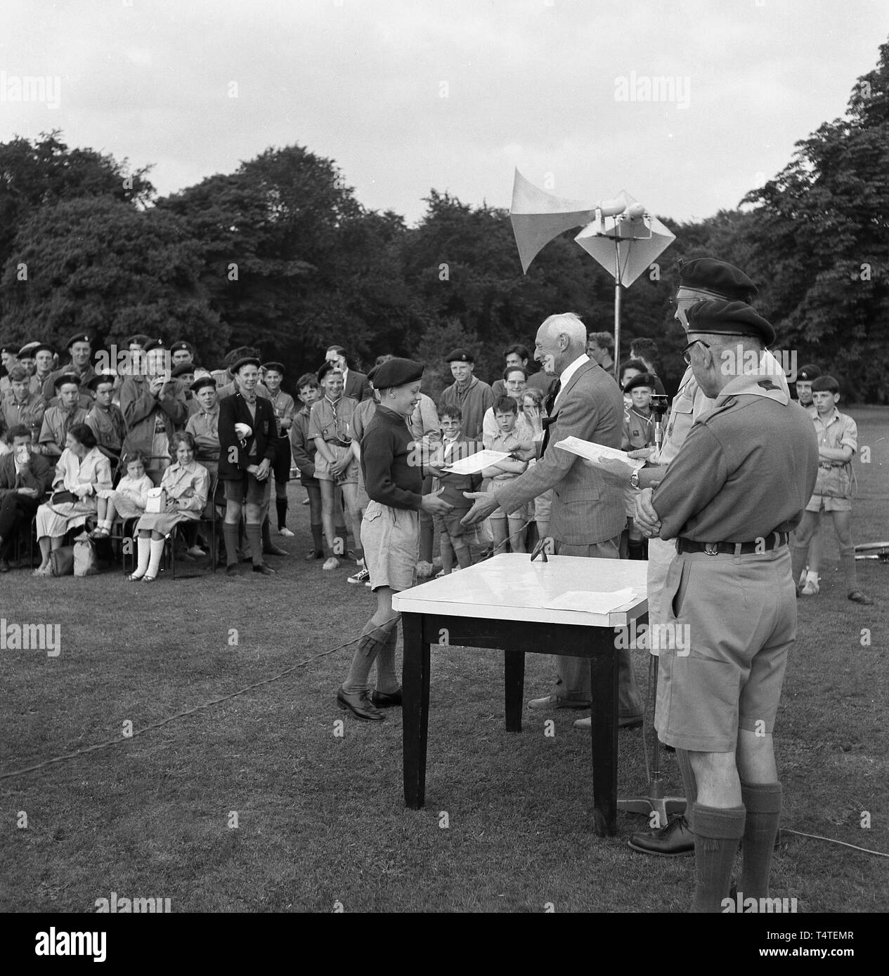 1960s. historical, outside in a field at a scouting ceremony, a young boy scout receiving a cub scout award achievement certificate from the scoutmaster and other team leaders at a table, England, UK. Stock Photo