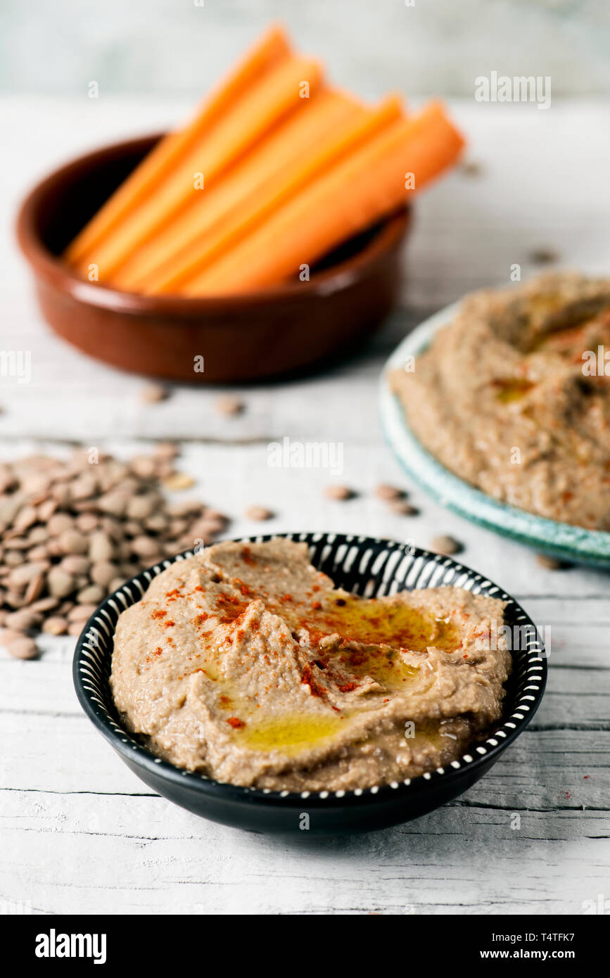 closeup of some different ceramic plates with homemade lentil hummus, seasoned with paprika, and a bowl with some strips of carrot to dip in, on a whi Stock Photo