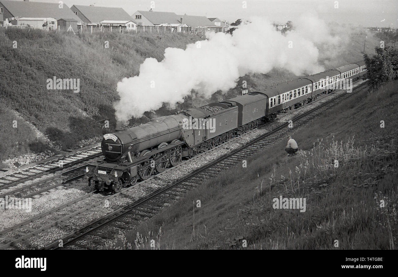 1969, historical, a man sitting on a grassbank by a railway track, watches as the iconic steam locomotive, The Flying Scotsman', goes past. Stock Photo