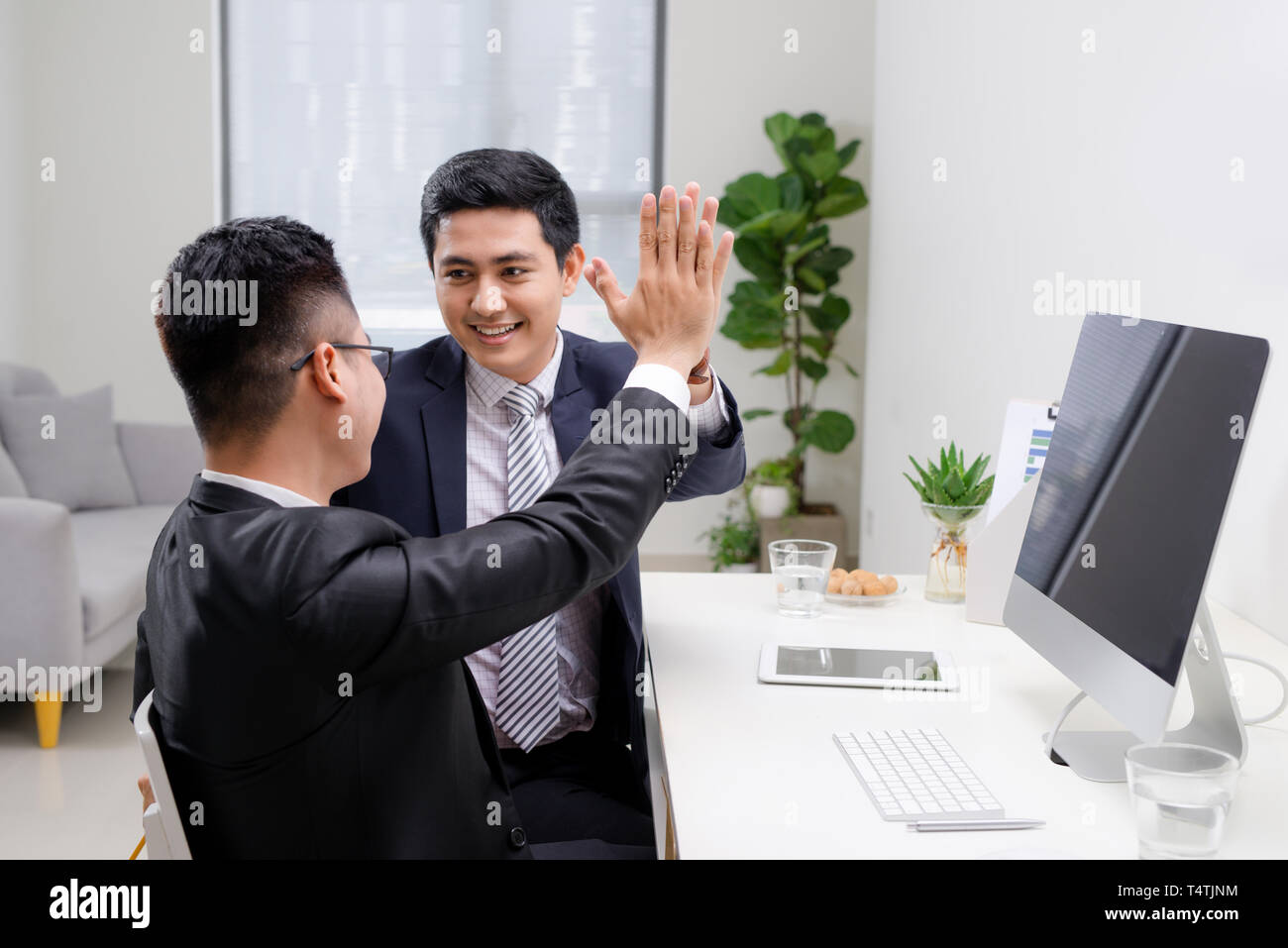 Two cheerful excited young men giving high five and working in office ...