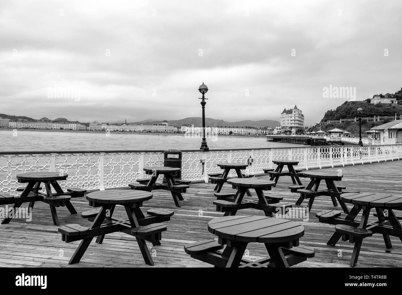Looking towards Grand Hotel and Llandudno promenade from pier with empty seats in black and white, North Wales UK Stock Photo