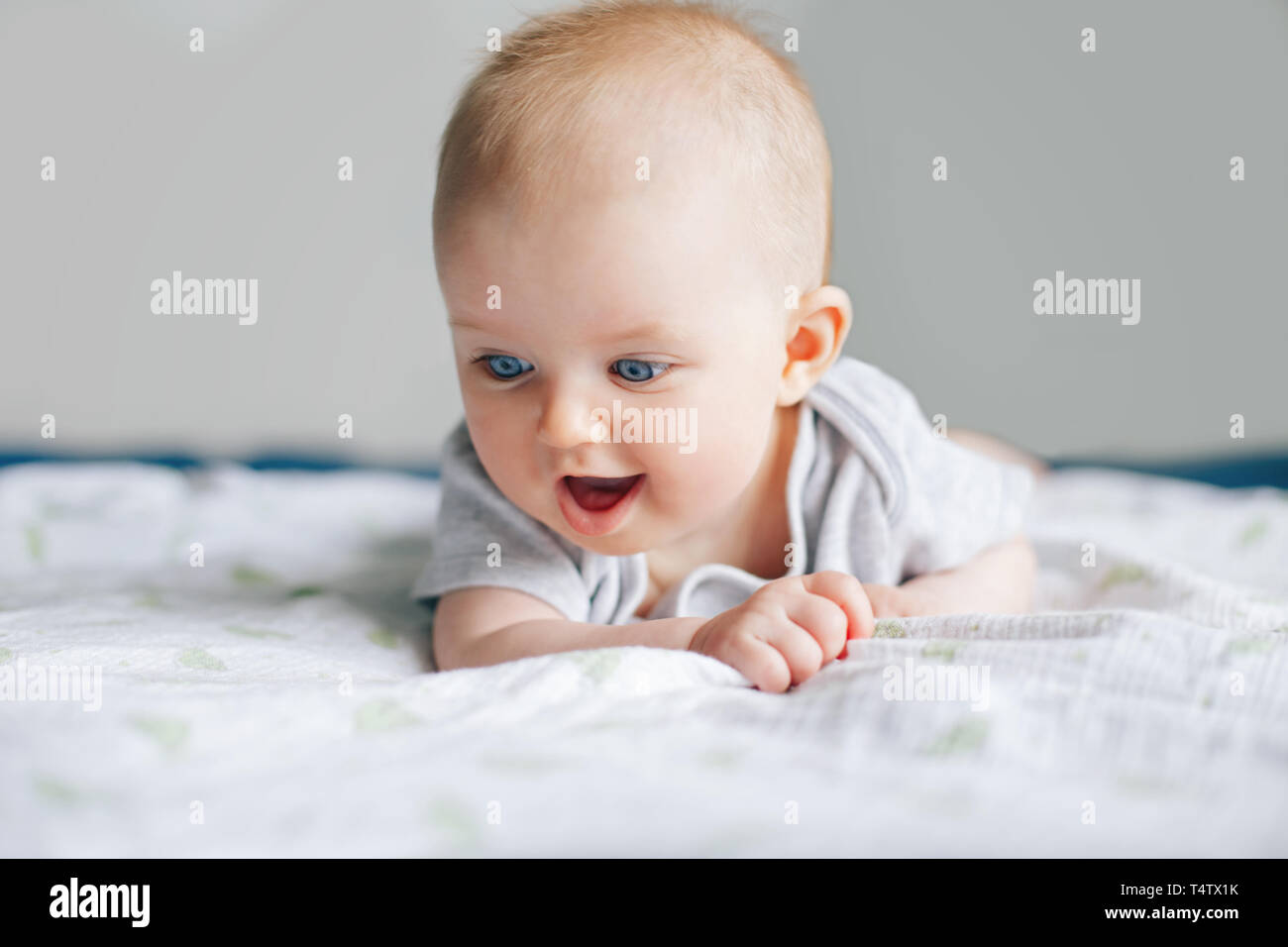 Closeup portrait of adorable funny white Caucasian baby with blue eyes  lying on tummy belly on bed. Aware cute newborn at home. Curious child boy  girl Stock Photo - Alamy