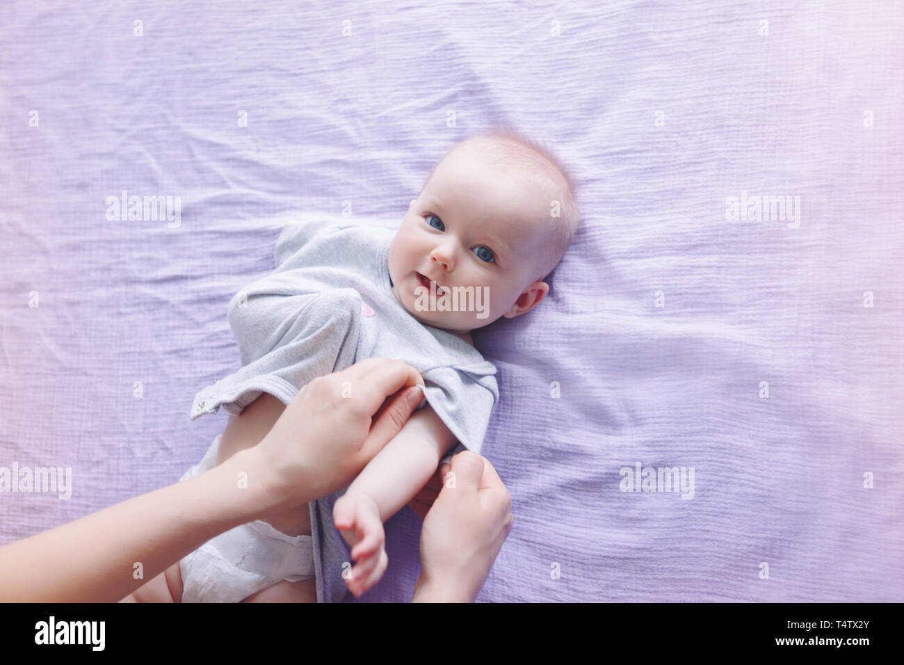 Parent nurse changing diaper for newborn baby daughter son child. Parent babysitter taking care of child and putting on clothes onesie. Authentic life Stock Photo