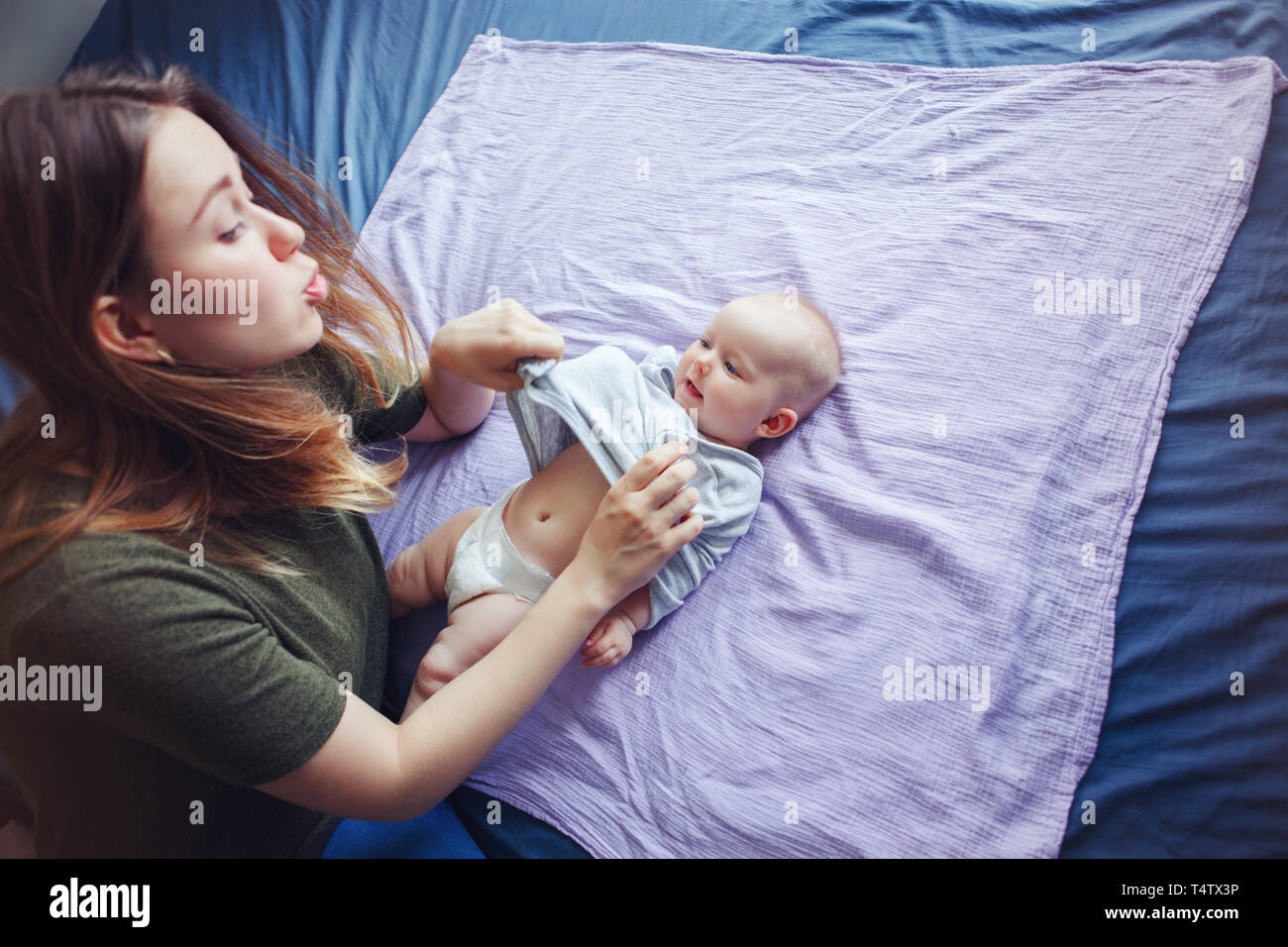 Young beautiful mother woman changing diaper for newborn baby daughter son child. Female parent taking care of child at home. Authentic lifestyle cand Stock Photo