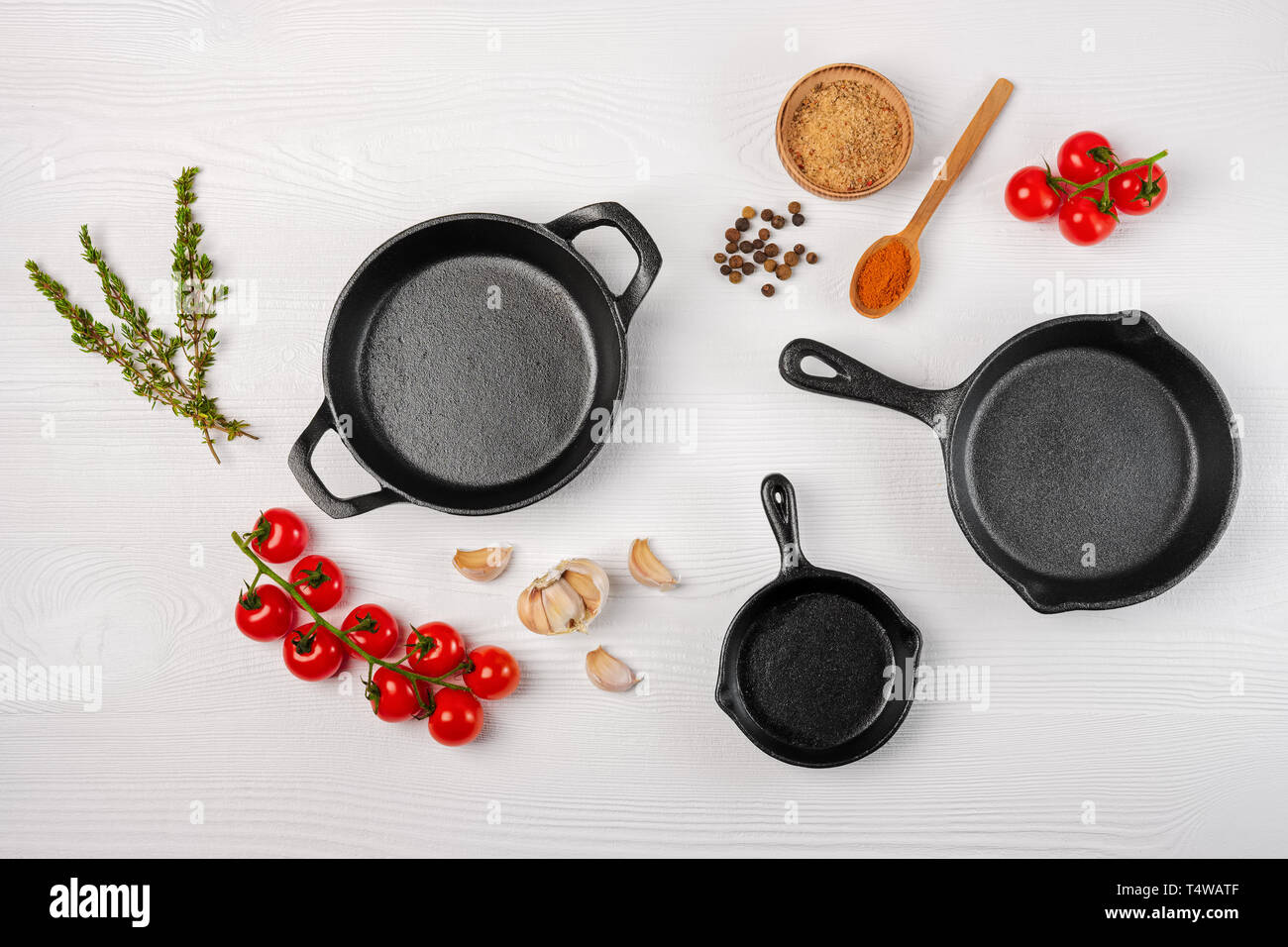 Cast iron skillets and spices on white wooden culinary background, view from above Stock Photo