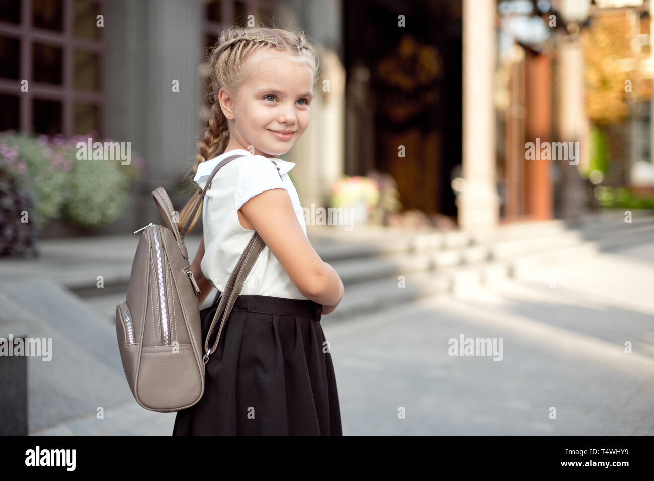 Happy smiling girl is going to school for the first time with bag go to elementary school. Pupil go study with backpack. Stock Photo