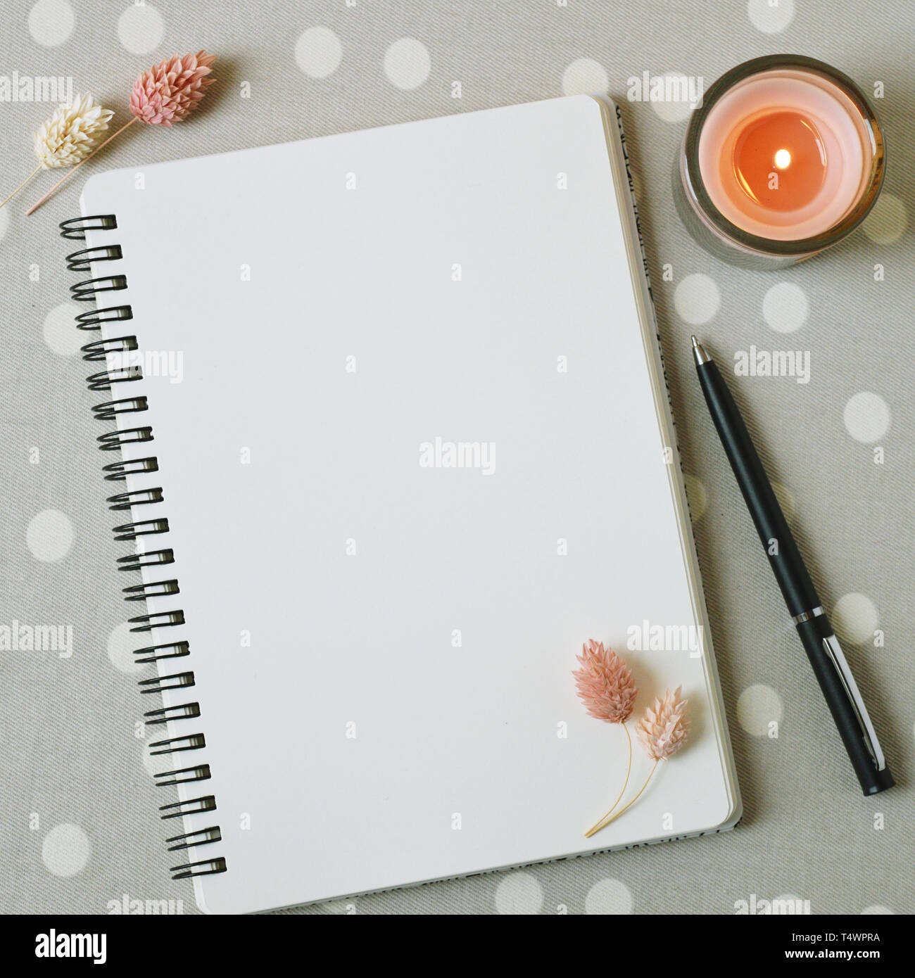 Empty page of notebook, dried flowers of pink tender color and coral candle. Planner for life goals. Lifestyle. Square photo. Grey table with white do Stock Photo